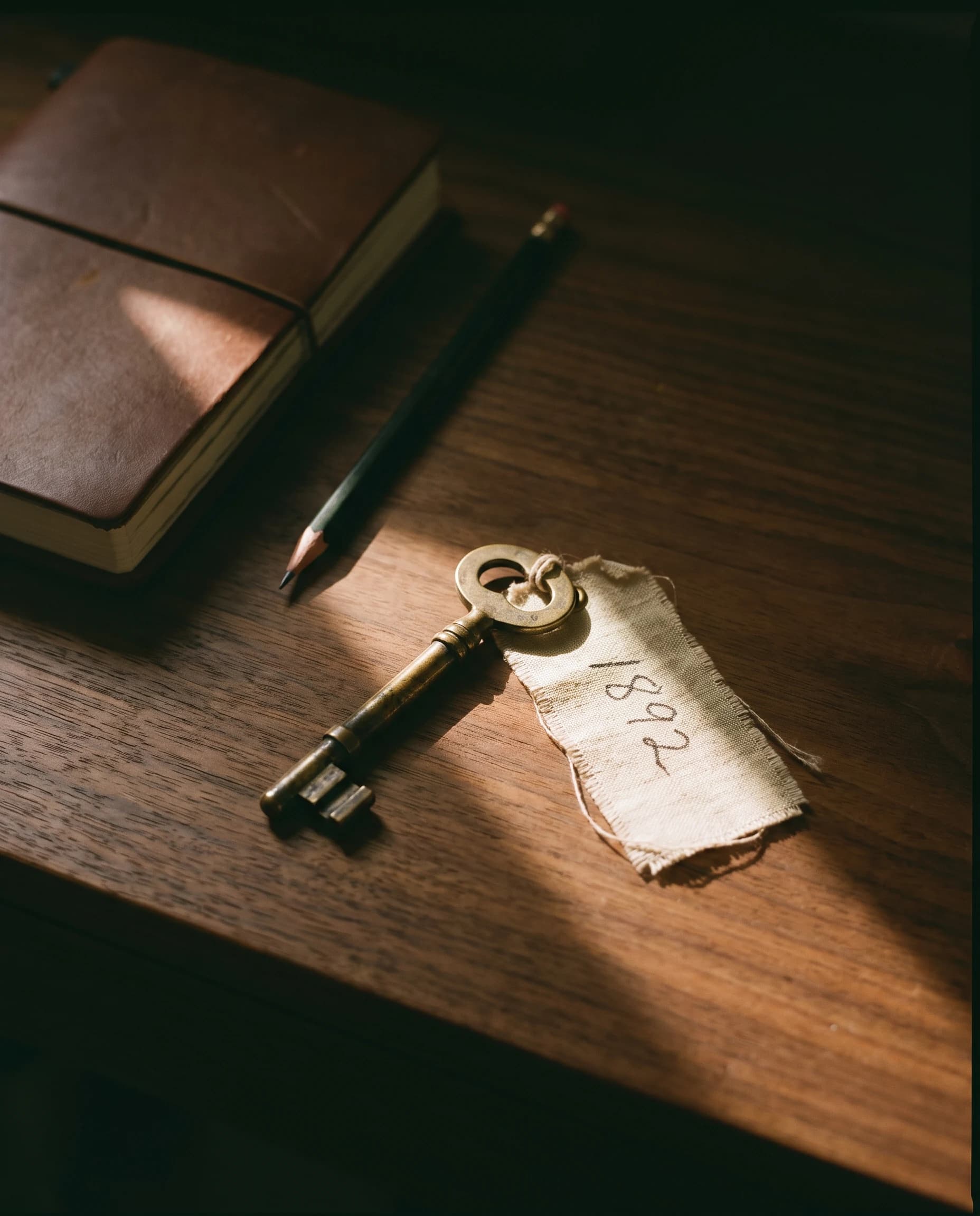 An old brass key with a paper tag on a desk beside a leather notebook